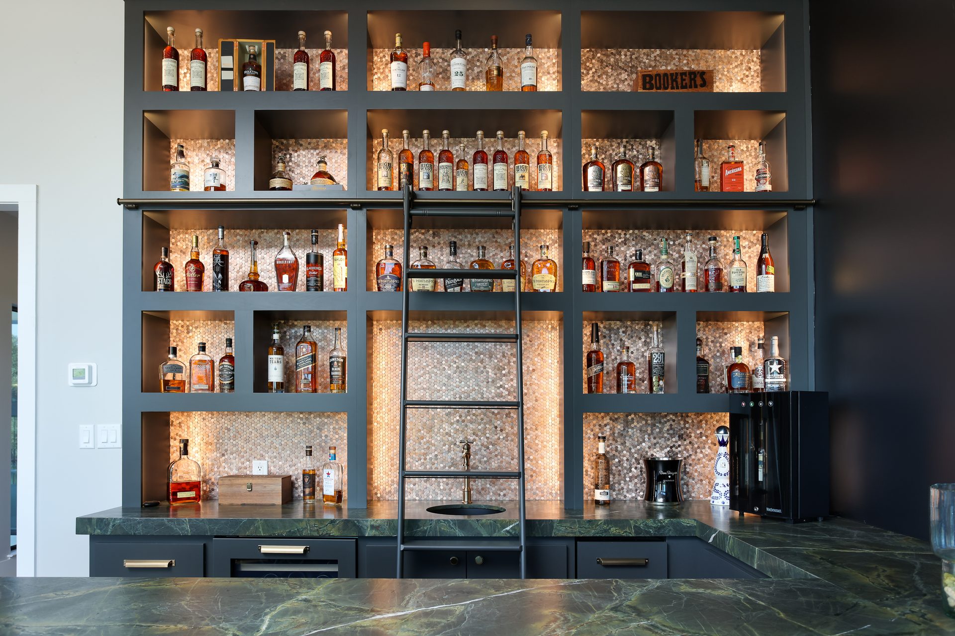 A custom home bar with backlit copper penny-tile shelving and a green marble counter